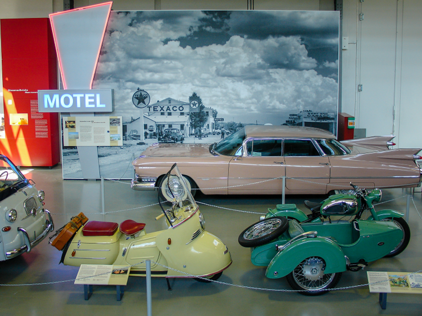 Impression vom "Reisen" in Halle II des Verkehrszentrums mit rosa Cadillac und Motorrollern