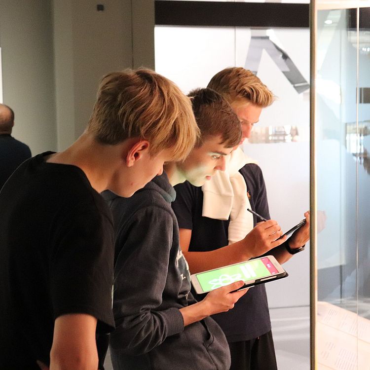 Schüler mit Tablet vor einer Vitrine in der Ausstellung Atomphysik.