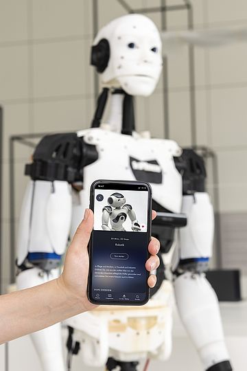 Hand hält ein Smartphone mit der Deutsches Museum App vor ein Exponat in der Ausstellung Robotik