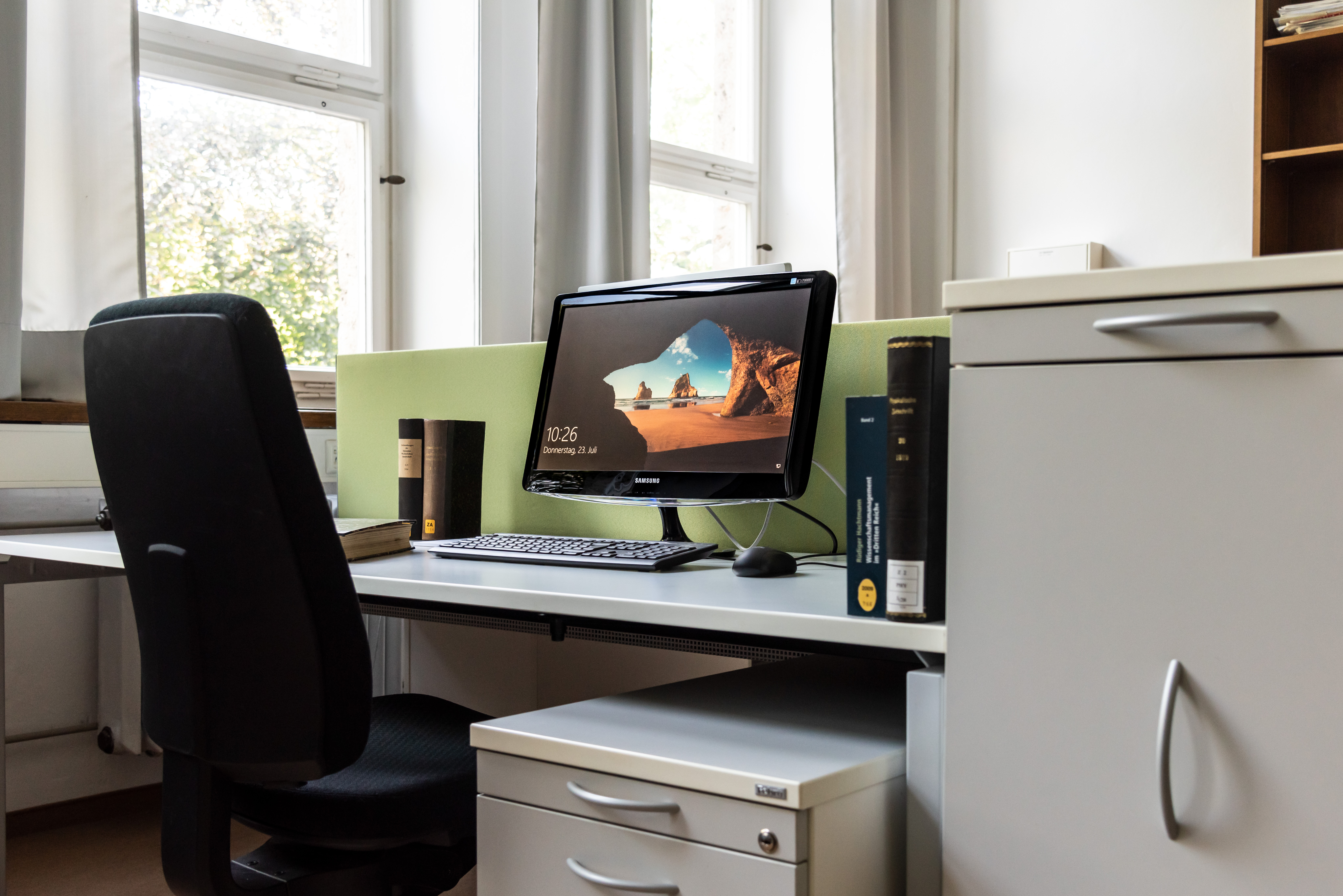 Arbeitsplatz eines Gastwissenschaftlers. Ein PC-Bildschirm und einige Bücher stehen auf dem Tisch.
