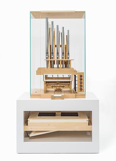 Dieses Bild zeigt das Orgelfunktionsmodell. Es handelt sich um einen Aufbau aus Holz, Metall und Plexiglas. Das Modell verfügt über einen Blasebalg im unteren Teil, fünf Tasten einer üblichen Klaviatur, ebenso viele Registerzüge, das sind Holzknöpfe zum Herausziehen, und einige Pfeifen aus Holz und Metall. 