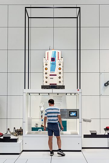 Besucher vor einer Vitrine mit Robotern zum Thema "Medizin und Pflege". Auf der Vitrine steht Roboter "HelpMate".