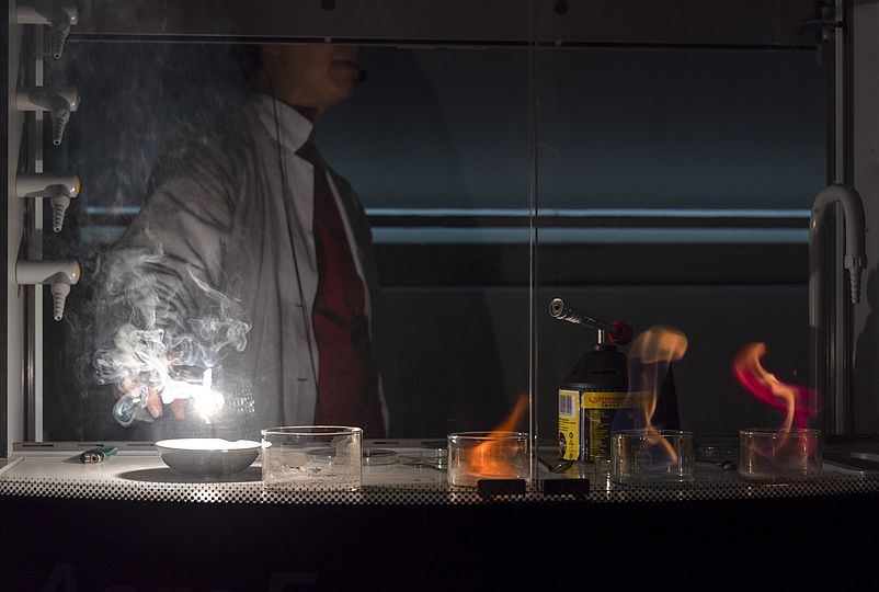 Eine Mitarbeiterin der Ausstellung Chemie zündet im Labor Salze an und eine weiße Flamme sticht empor.