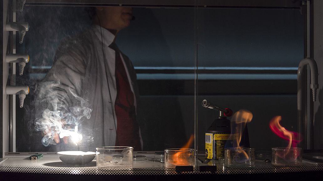 Eine Mitarbeiterin der Ausstellung Chemie zündet im Labor Salze an und eine weiße Flamme sticht empor.
