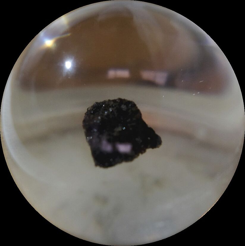 Ein schwarzes, kleines Stück Mondgestein hinter Plexiglas