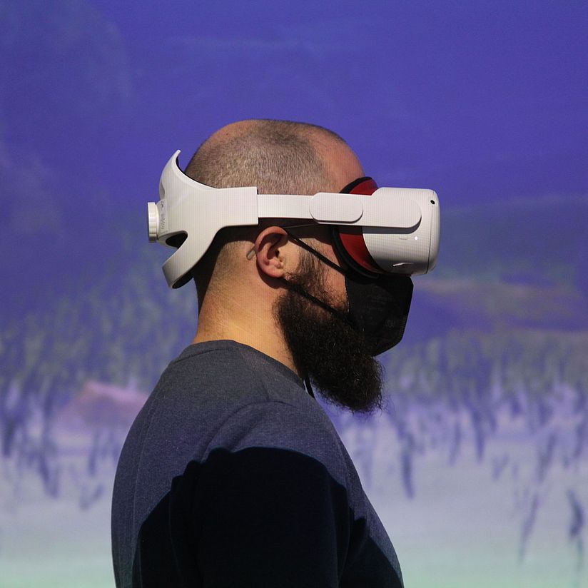 Person mit VR Brille Foto einer Person im Profil vor einer Projektionsfläche mit einer FFP 2 Maske und einer VR Brille auf dem Kopf