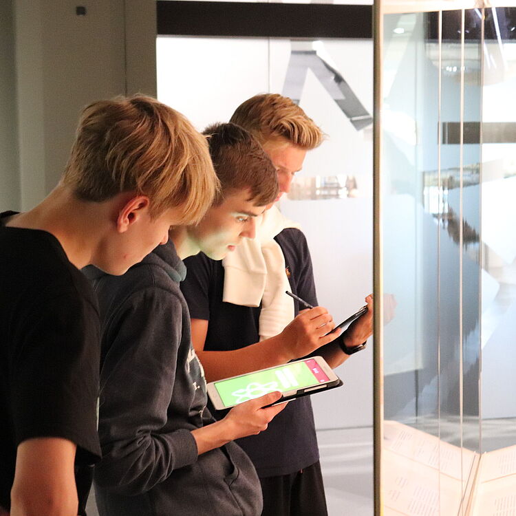 Schüler mit Tablet vor einer Vitrine in der Ausstellung Atomphysik.