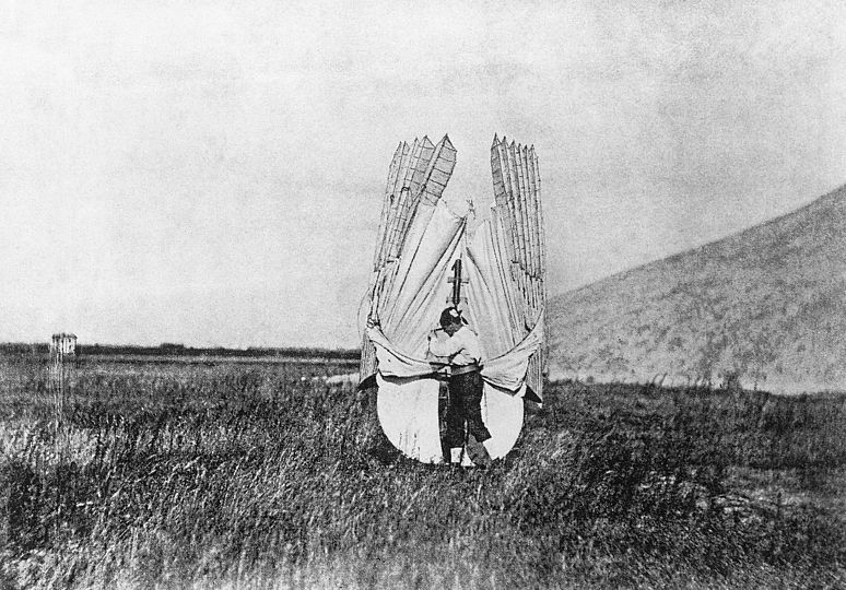 Otto Otto Lilienthal steht am Fuß des Fliegebergs und trägt den Gleiter mit hochgeklappten Flügeln auf seinem Rücken.