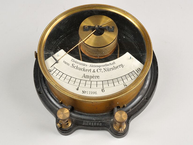 Farbfotografie von Amperemeter. Messingfarben und Schwarz. Anzeige in weiß von 0 bis 10 Ampere mit Zeiger.