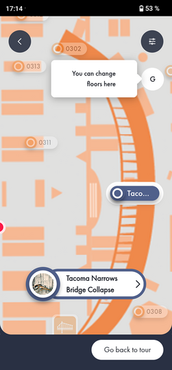 Smartphone-Screenshot einer Museums- oder Ausstellungs-Map-App: zentral orangefarbene stilisierte Brücken-Illustration mit markierten Punkten (0302, 0311, 0313, 0308), Sprechblase oben mittig mit englischem Hinweis "You can change floors here", runder Button "G" rechts, hervorgehobene Karte-Markierung und blaue Infokarte unten mittig mit Miniaturbild und Titel "Tacoma Narrows Bridge Collapse", unten rechts weißer Button "Go back to tour" sowie Statusleiste oben mit Uhrzeit 17:14 und Akkuanzeige 53 %.