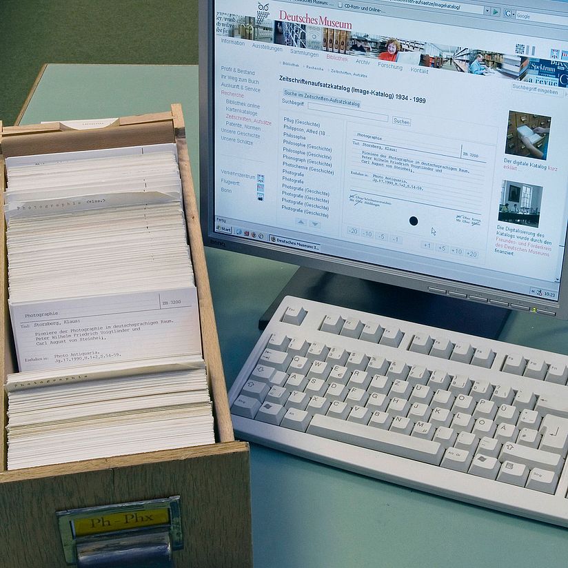 Die Zettelkataloge werden nach und nach in den Online-Katalog eingearbeitet. Kasten mit Katalogkarten neben einem Bildschirm
