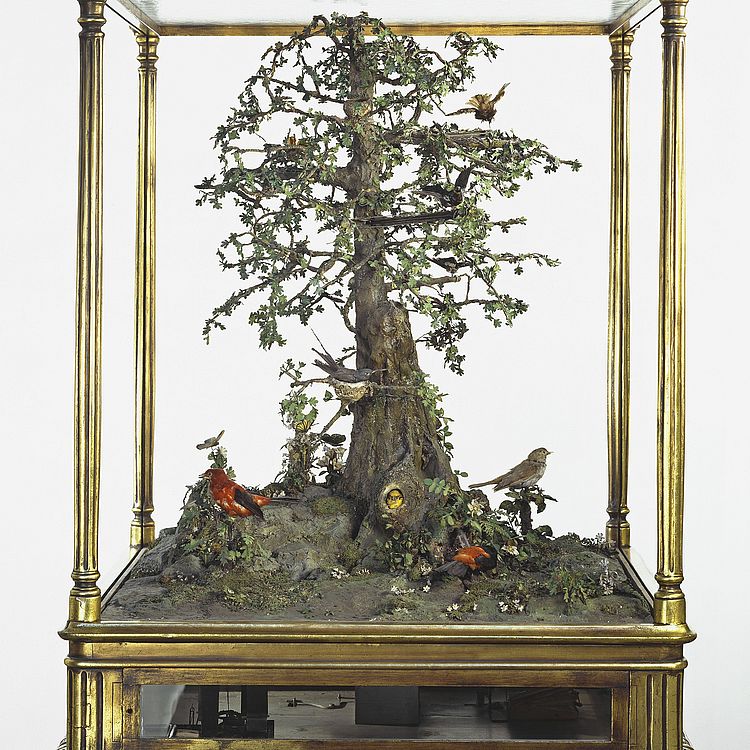 Großer Musikautomat in Kastenformat, mit einen Baum und Vögeln.