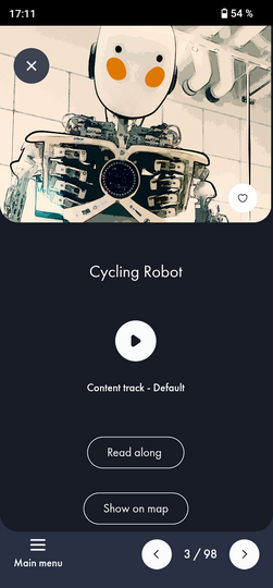 Screenshot einer Museums-App: oben eine stilisierte Roboterfigur mit rundem weißem Kopf und orangefarbenen Wangen in einem Ausstellungsraum, Titeltext "Cycling Robot", mittig ein Play-Button, darunter die Beschriftung "Content track - Default" sowie zwei abgerundete Buttons "Read along" und "Show on map"; unten Navigationsleiste mit "Main menu" und Seitenanzeige "3 / 98".