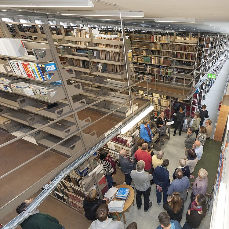 Personen nehmen an einer Bibliotheksführung im Magazin teil.