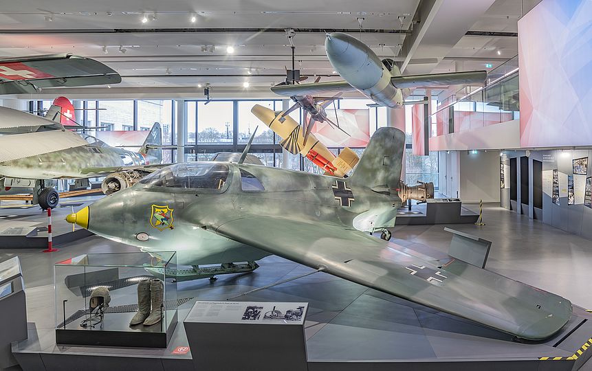 Flugzeug Messerschmitt Me 163 in der Ausstellung Historische Luftfahrt. Auf dem Podest befindet sich in einer kleine Vitrine mit einem Paar Überziehstiefel und einer Fliegerhaube für Piloten der Me 163.