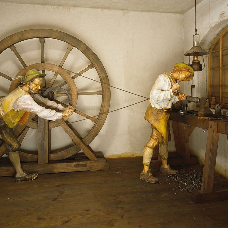 Das Bild zeigt ein Modell einer Drehbank mit Radantrieb (18. Jh.), über den ein Gehilfe das zu bearbeitende Werkstück in Bewegung versetzt.