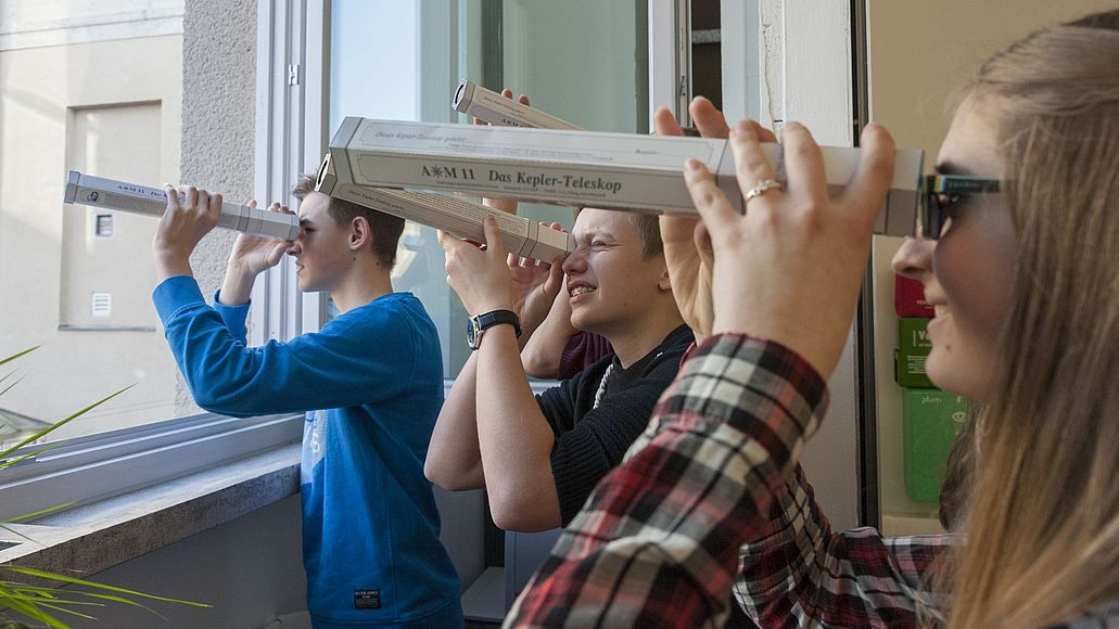 Teilnehmer*innen schauen durch selbstgebaute Teleskope.