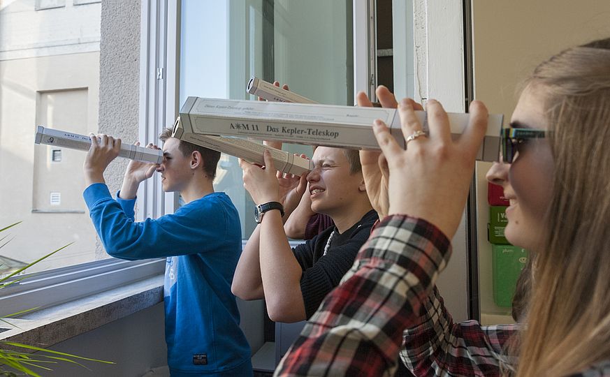 Teilnehmer*innen schauen durch selbstgebaute Teleskope.