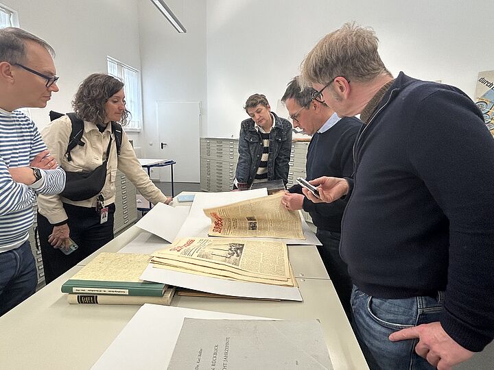 Fünf Personen stehen in einem Raum des Archivs, wo Originalquellen ausgelegt sind..