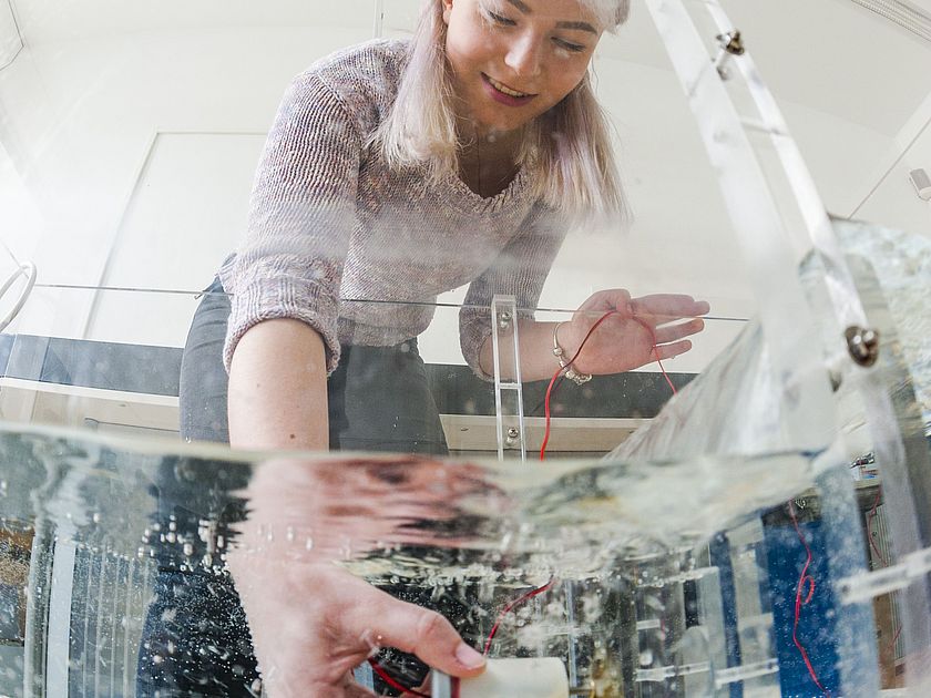Experimentieren zur Wasserkraft Eine junge Frau hält eine Turbine in ein durchsichtiges Wasserbecken.