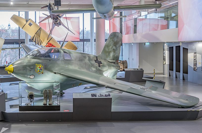 Flugzeug Messerschmitt Me 163 in der Ausstellung Historische Luftfahrt. Auf dem Podest befindet sich in einer kleine Vitrine mit einem Paar Überziehstiefel und einer Fliegerhaube für Piloten der Me 163.