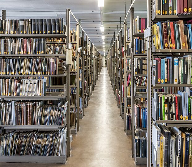 Blick in einen Gang im Magazin der Bibliothek des Deutschen Museums, der von Bücherregalen gesäumt ist.