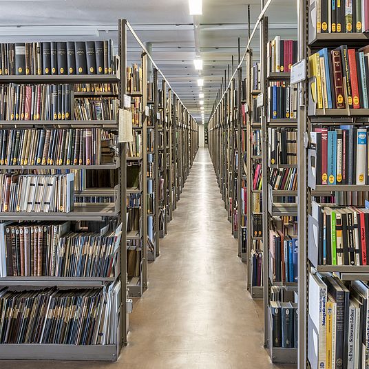 Blick in einen Gang im Magazin der Bibliothek des Deutschen Museums, der von Bücherregalen gesäumt ist.