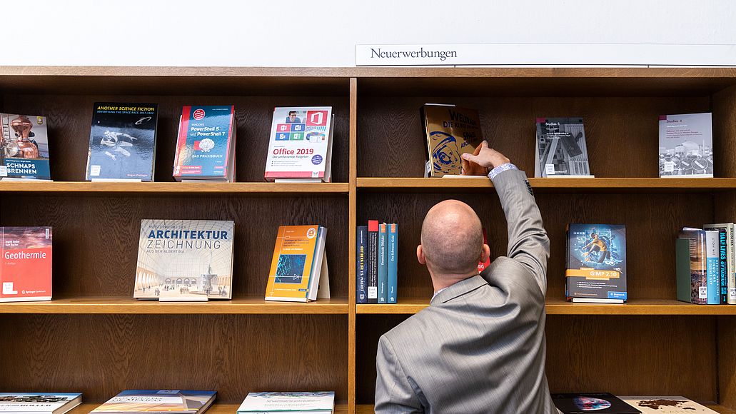 Neuerwerbungsregal Ein Nutzer nimmt ein Buch aus dem Neuerwerbungsregal.