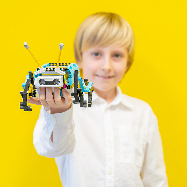 Junge hält kleinen Roboter in der Hand.