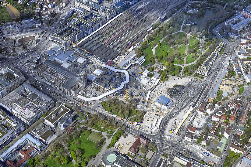 Die Luftaufnahme zeigt einen Überblick über die Stuttgarter Innenstadt rund um den Hauptbahnhof. In der Bildmitte liegt die große Baustelle des neuen Hauptbahnhofs. Rechts davon liegen die Gleise des alten Kopfbahnhofs. Links im Bild befindet sich die Innenstadt mit der Königstraße. Anschließend an den Bahnhof im Bild unten befindet sich der Schlossgarten.