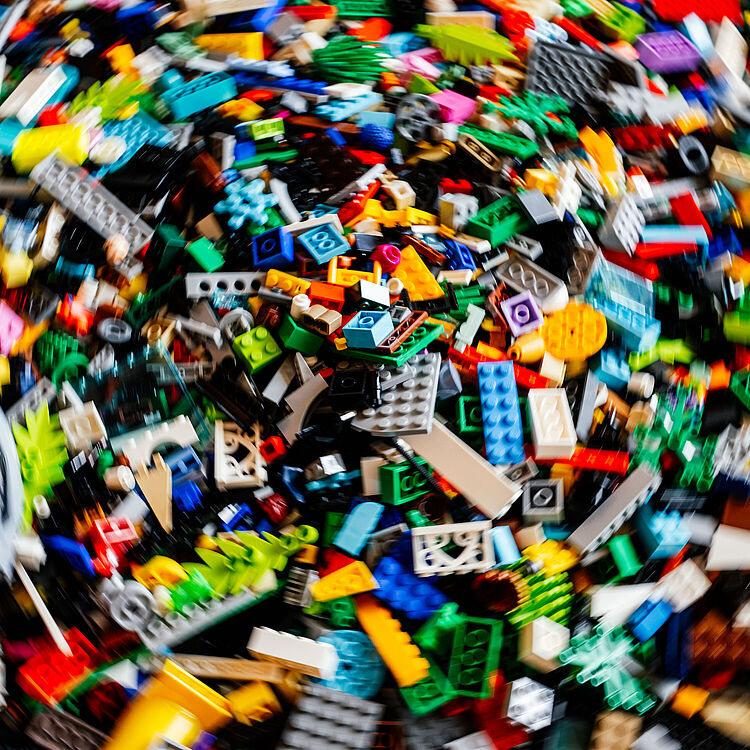 Buntes Durcheinander aus vielen kleinen LEGO-Steinen und -Teilen in verschiedenen Formen und Farben, unscharf fotografiert als großer Haufen.