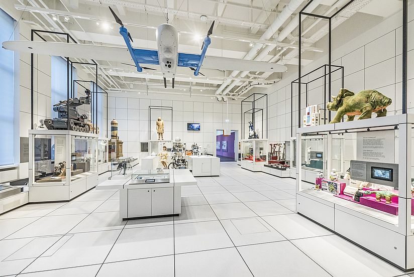 Ein Raum, in dem Boden, Decke und Wänre weiß sind, stehen verscheidenen Vitrinen mit Robotern aus unterschiedlichen Jahrhunderten.