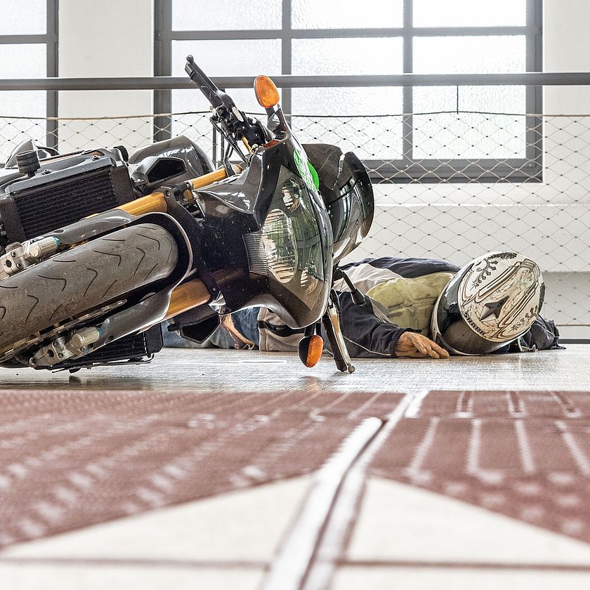 Eine Motorradfahrerpuppe liegt neben einer umgekippten Maschine