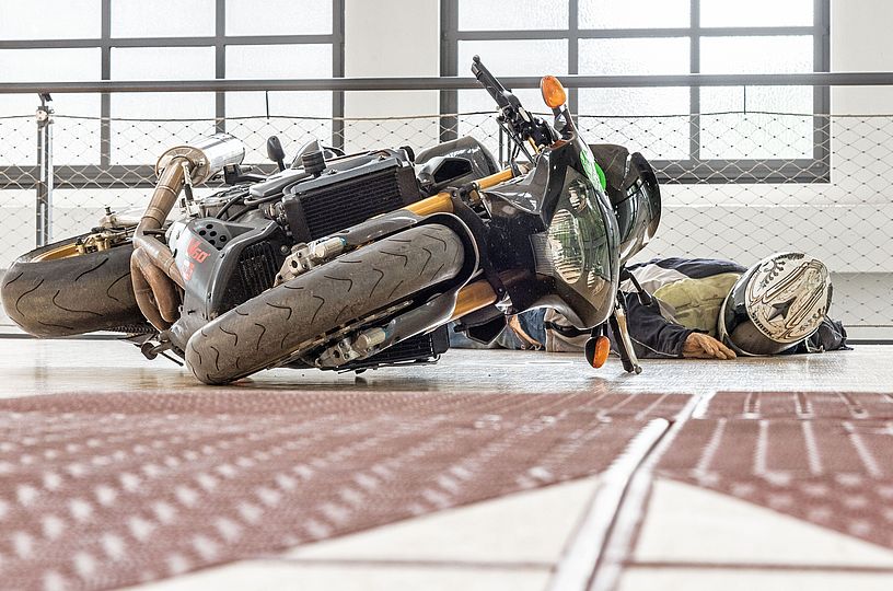 Eine Motorradfahrerpuppe liegt neben einer umgekippten Maschine