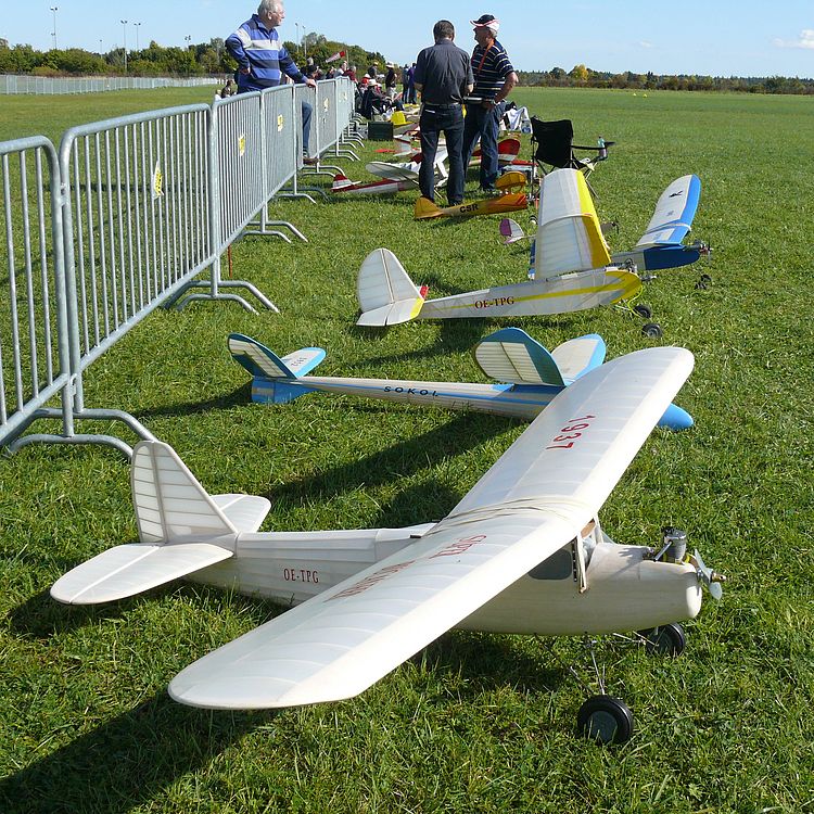 Oldtimer-Modellflugtag in der Flugwerft Schließheim. Zu sehen sind einige Modellflugzeuge und interessierte Besucherinnen und Besucher.