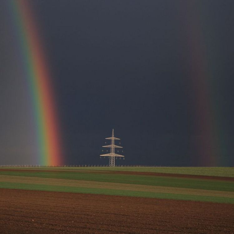 Feld mit Strommast und Regenbogen.