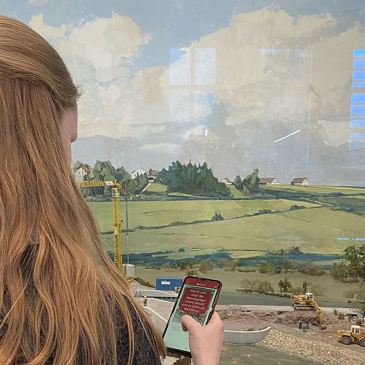 Jugendliche steht mit ihrem Smartphone vor einem Diorama der Ausstellung Landwirtschaft- und Ernährung.