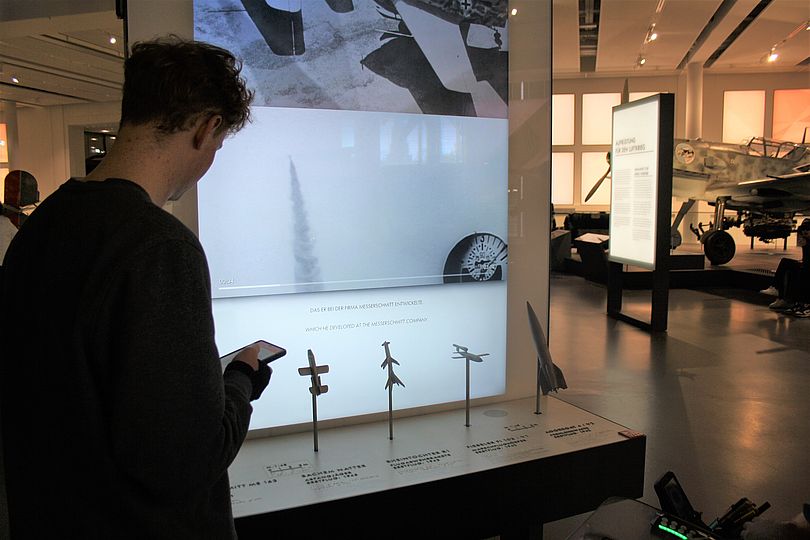 Schüler steht vor den Tastmodellen Abfangjäger Messerschmitt ME 163, Abfangjäger Bachem Natter, Flugabwehrrakete Rheintochter R1, Marschflugkörper Fieseler Fi 103 / V1 und  Fernlenkwaffe Aggregat 4 / V22.