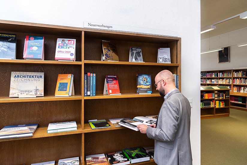 Eine Person steht am Neuerwerbungsregal im Lesesaal der Bibliothek.