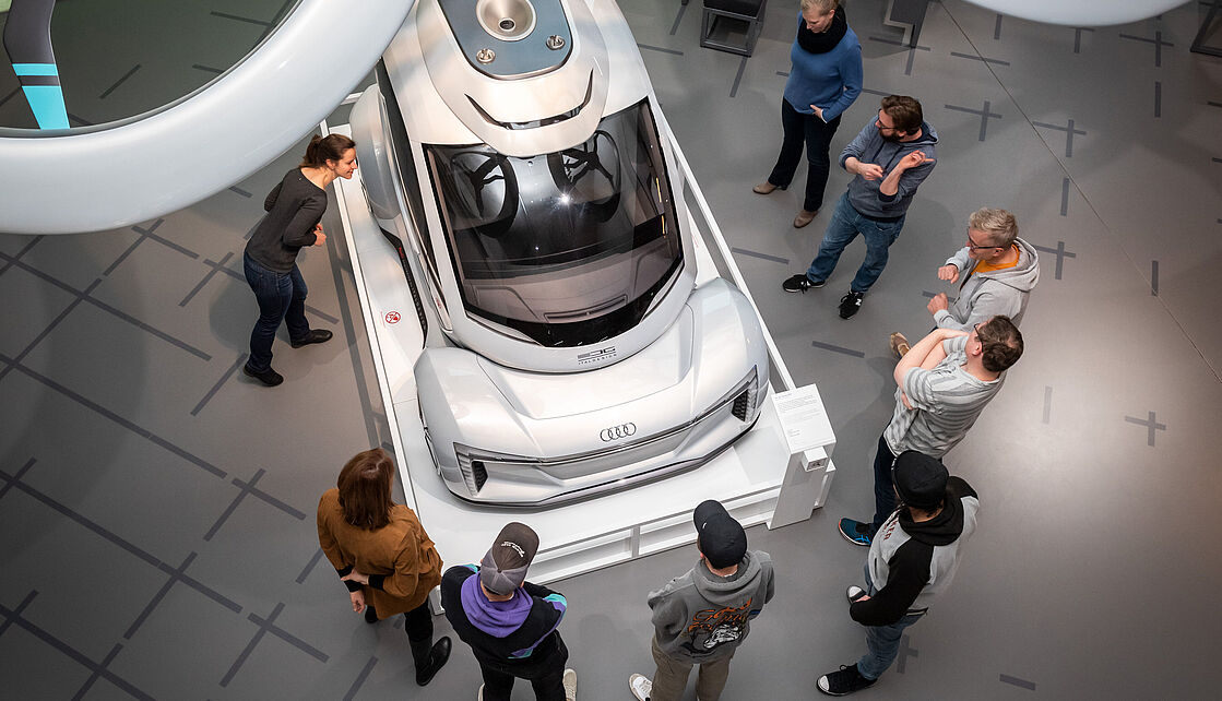 Tour durchs Deutsche Museum Nürnberg. Eine Gruppe von Menschen steht bei einer Tour durchs Museum vor einem Exponat.