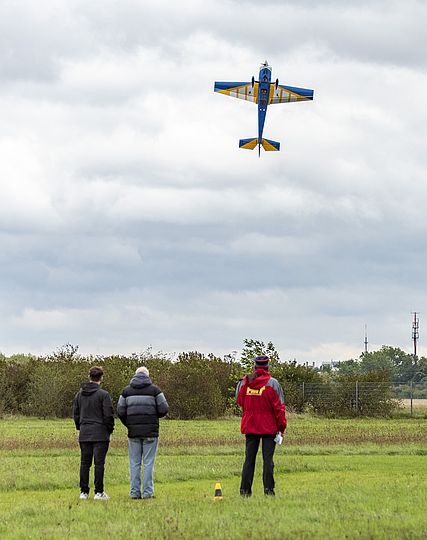 Drei Personen und ein fliegendes Modellflugzeug.