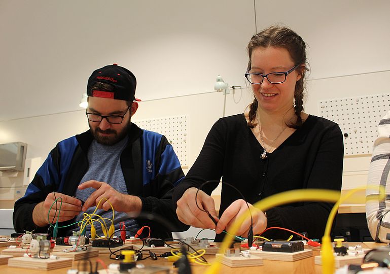 Zwei junge Erwachsene bauen mit unterschiedlichen Elementen Stromkreise zusammen.