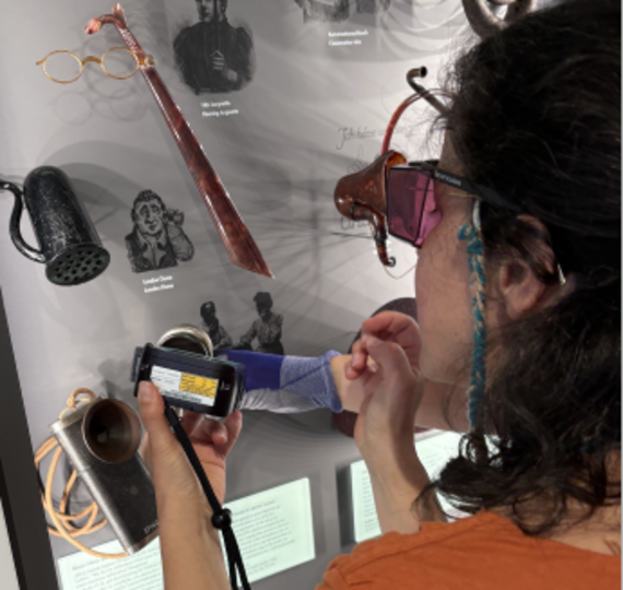 Objekte auf Tisch werden von Frau mit Lupenbrille untersucht