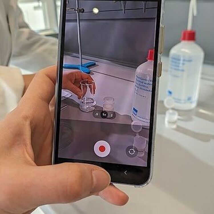 Hand mit Smartphone filmt einen chemischen Versuch.