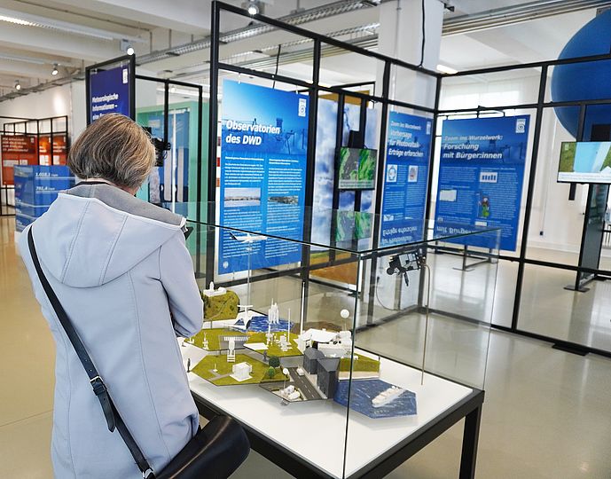 Besucherin betrachtet das Modell eines Messfeldes in einer Tischvitrine.