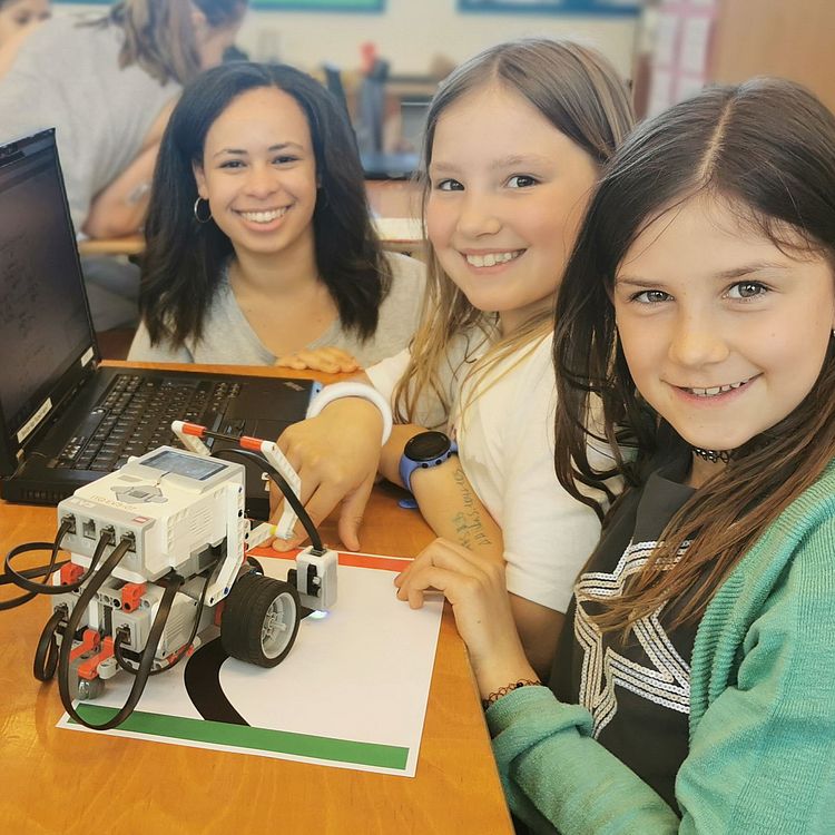 Drei Mädchen mit einem Lego-Mindstorm Roboter vor einem aufgeklappten Laptop.