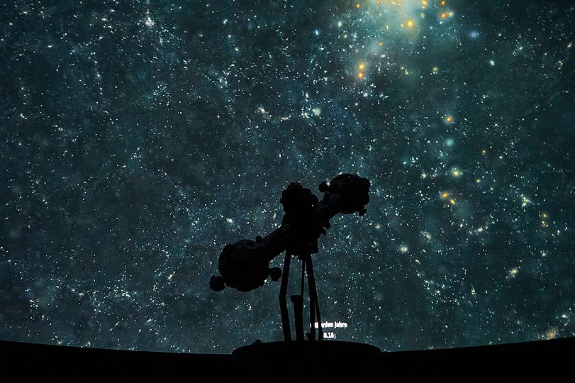 Zeiss Refraktor im Planetarium. Im Hintergrund eine Projektion des Nachthimmels.
