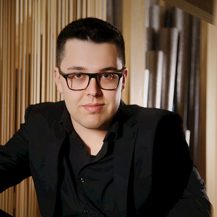 Mattia Rosati sitzt vor einer Orgel und schaut in die Kamera
