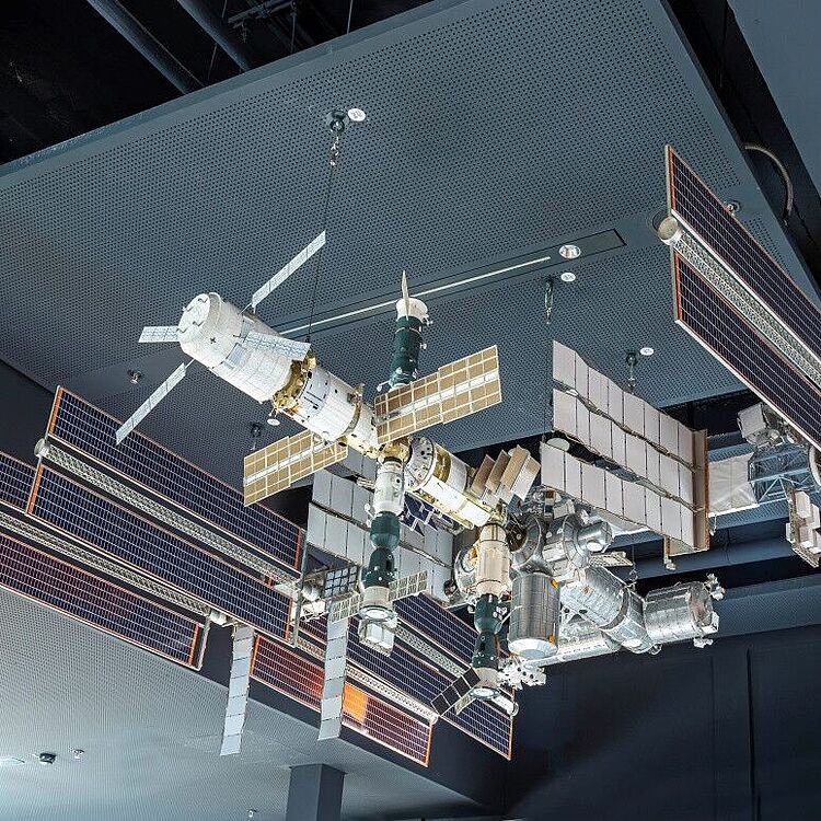 Detailliertes Modell der Internationalen Raumstation (ISS) mit ausgebreiteten Solarpanelen und angedockten Modulen, hängend unter einer Ausstellungshalle-Decke.