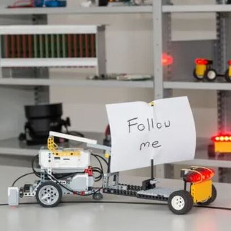 Selbsterstellte kleine elektronischen Fahrzeuge aus Lego-Technik, dahinter ein Regal mit weiteren kleinen Fahrzeugen